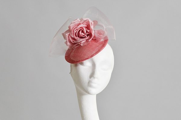 Candy Pink button Hat with silk flower and crinoline bow sited on front left of models head and model looking to camera while facing to the right